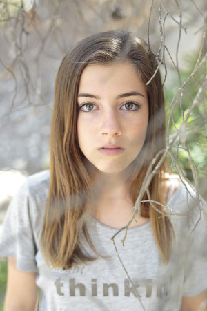 Face of a girl among branches of a tree with green leavesの写真素材