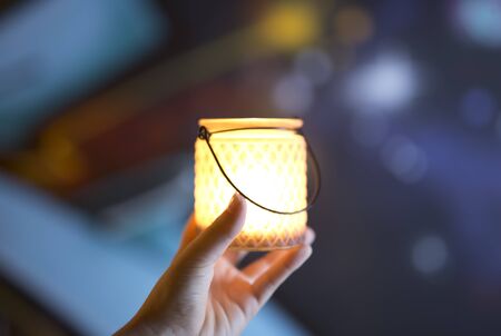 Container glass in the hand of a young woman, with a candle lit inside. Horizontal shot with colors out of focus background.の写真素材