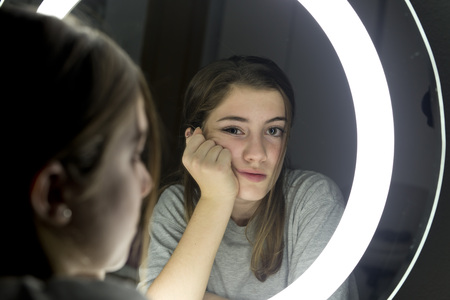 Portrait of teenage looking in a mirror, with the sad and serious face. horizontal shot.の写真素材
