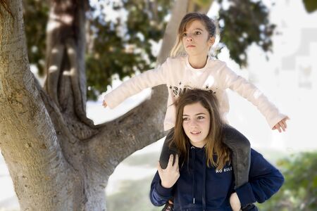Girl climb on the shoulders of his sister, making games a sunny autumn day.