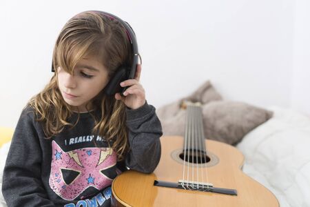 Little girl learning to play classical guitar, sitting on her bed.の写真素材