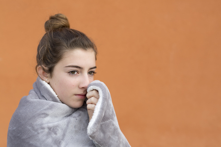 Portrait of a girl covered with a blanket, on an orange background. Horizontal shot with natural light.の写真素材