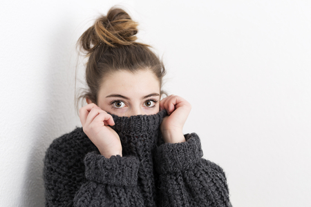 Young woman covering her mouth with a sweater on a white background. Horizontal shot with studio light.の写真素材