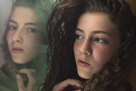 Teenage woman looking at herself in a mirror with serious face.の写真素材
