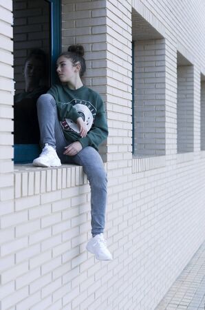 Teen girl sitting in the window of a building. Vertical shot with natural light.の写真素材