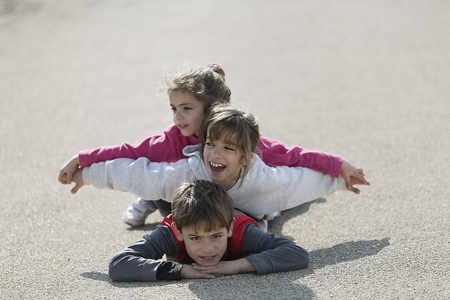 Three children lying on the floor one on top of the other.  Horizontal shot with natural lightの写真素材