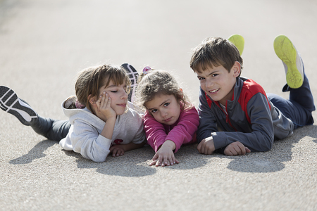Three children lying on the ground of a road facing the camera. Horizontal shot with natural lightの写真素材