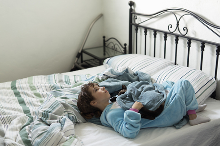 10 year old girl lying down and thinking about the bed with her cat on top. Horizontal shot with natural light.の写真素材