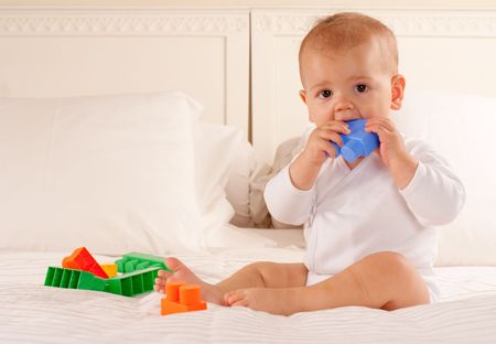 
Cute baby sitting o an a bed biting a colourful toy brick
の写真素材