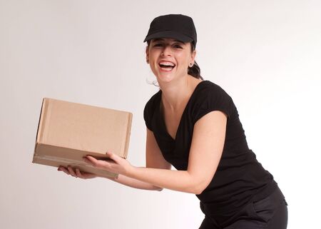 Portrait of a laughing delivery girl in black carrying a parcelの写真素材