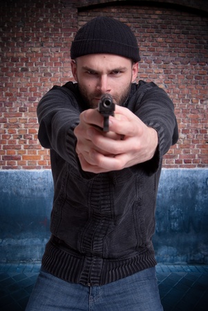 

Dangerous looking man holding a gun aiming at you in an urban background

の写真素材