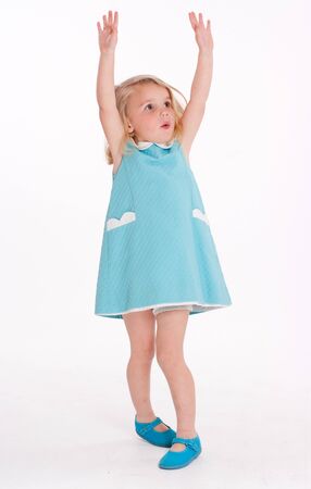 Cute little blonde girl in a blue summer dress with her arms raisedの写真素材