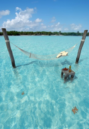 Hammock hanging over tropical sea water, and a table with refreshmentsの写真素材