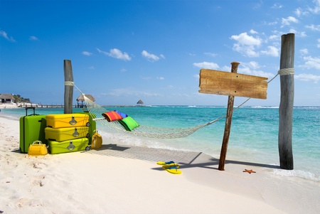 A hanging hammock, a wooden sign post , a pile of luggage, thongs and starfish on a beach resortの写真素材
