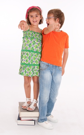A boy and a little girl standing on a top of books, smiling and pointing at the cameraの写真素材