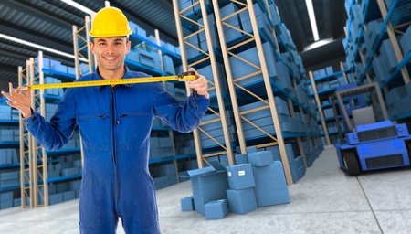 Man with helmet and blue overalls in a distribution warehouse extending a tape measure in blue shadesの写真素材
