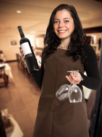 Smiling female sommelier presenting a wine bottle with a blank label and a pair of glasses in a restaurantの写真素材