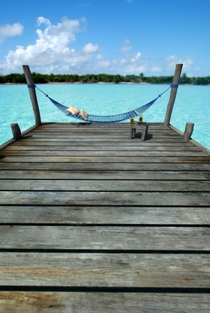 Hammock swinging in a pier by a tropical landscape, with a side table laden with fruits and refreshmentsの写真素材