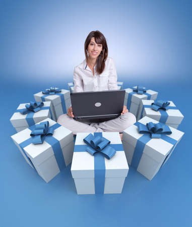 Young girl sitting with a laptop surrounded by gift boxesの写真素材