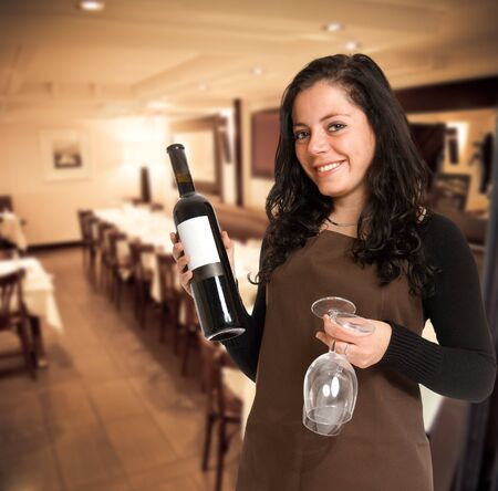 Smiling female sommelier presenting a wine bottle with a blank label and a pair of glasses in a restaurantの写真素材