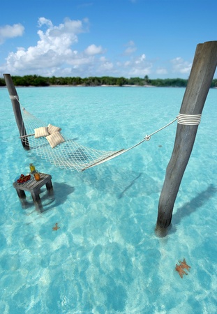 Hammock hanging over tropical sea water, and a table with refreshmentsの写真素材