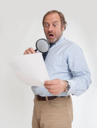 

Man with a shocked expression analyzing a document through a magnifying glass

の写真素材