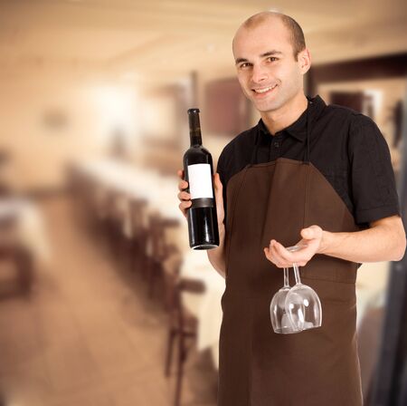 Smiling sommelier presenting a wine bottle with a blank label and a pair of glasses in a restaurantの写真素材
