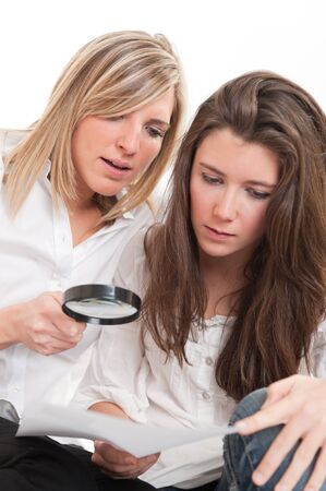 A pair of beautiful young women examining a document thou a magnifying glassの写真素材