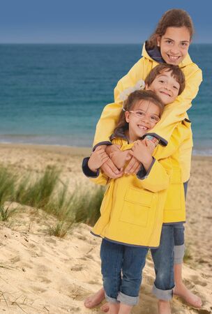 Three happy kids in raincoats on the beachの写真素材