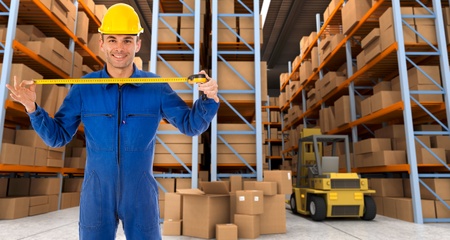 Man with helmet and blue overalls in a distribution warehouse extending a tape measureの写真素材