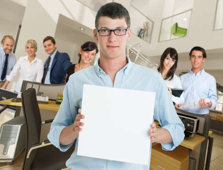 Young man holding a blank sign in an office with a supporting teamの写真素材