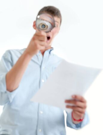 Young man with shocked expression examining a document through a magnifying lensの写真素材