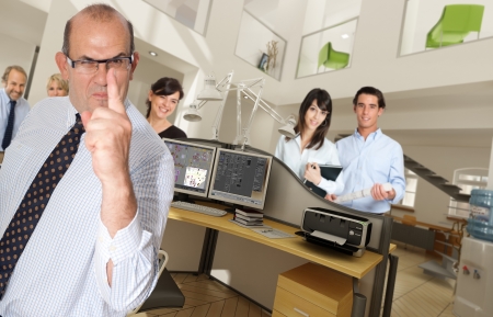 Humorous shot of a menacing business man in an office surrounded by smiling workersの写真素材