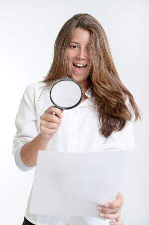 Young woman with a happy expression examining a document with a magnifying glassの写真素材