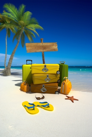 Pile of luggage by a wooden sign on a tropical beachの写真素材