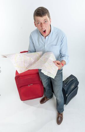 Desperate young man holding a map  surrounded by luggage の写真素材