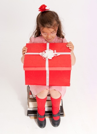 
A little girl sitting on a pile of books opening the lid of a big present
の写真素材