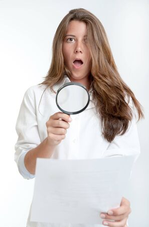 Young woman with a shocked expression examining a document with a magnifying glassの写真素材