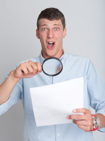 Young man with shocked expression examining a document through a magnifying lensの写真素材