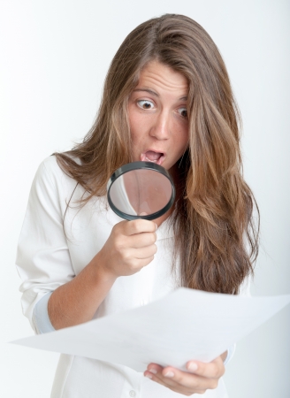 Young woman with a shocked expression examining a document with a magnifying glassの写真素材