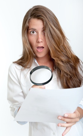 Young woman with a shocked expression examining a document with a magnifying glassの写真素材