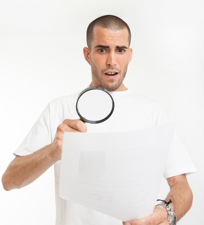 Young man reading a document through a magnifying glass with a shocked expressionの写真素材