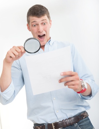 Young man with shocked expression examining a document through a magnifying lensの写真素材
