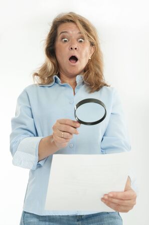 Woman with shocked expression examining a document thru a magnifying glassの写真素材