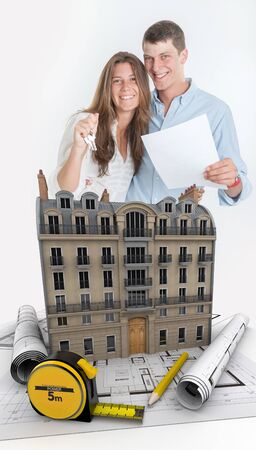 Young couple happily holding a contract and a bunch of keys with a building and blueprints