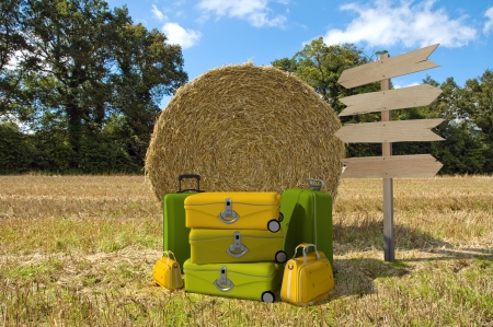 A pile of luggage with directional signs pointing everywhere in the middle of a field with hay balesの写真素材