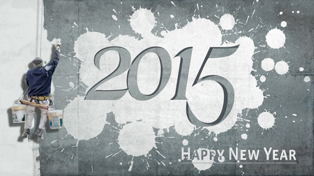 Building painter hanging from harness painting a wall with the words Happy New Year 2015