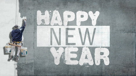 Building painter hanging from harness painting a wall with the words Happy New Year