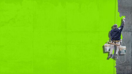 Building Painter hanging from harness painting a wall in bright green with lots of copy space for your own, messageの写真素材
