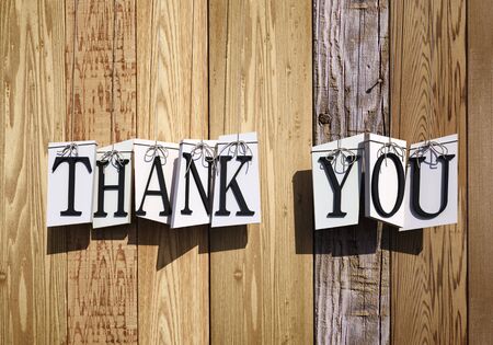 3D rendering of letters forming the words thank you hanging from strings against a wooden planks backgroundの写真素材